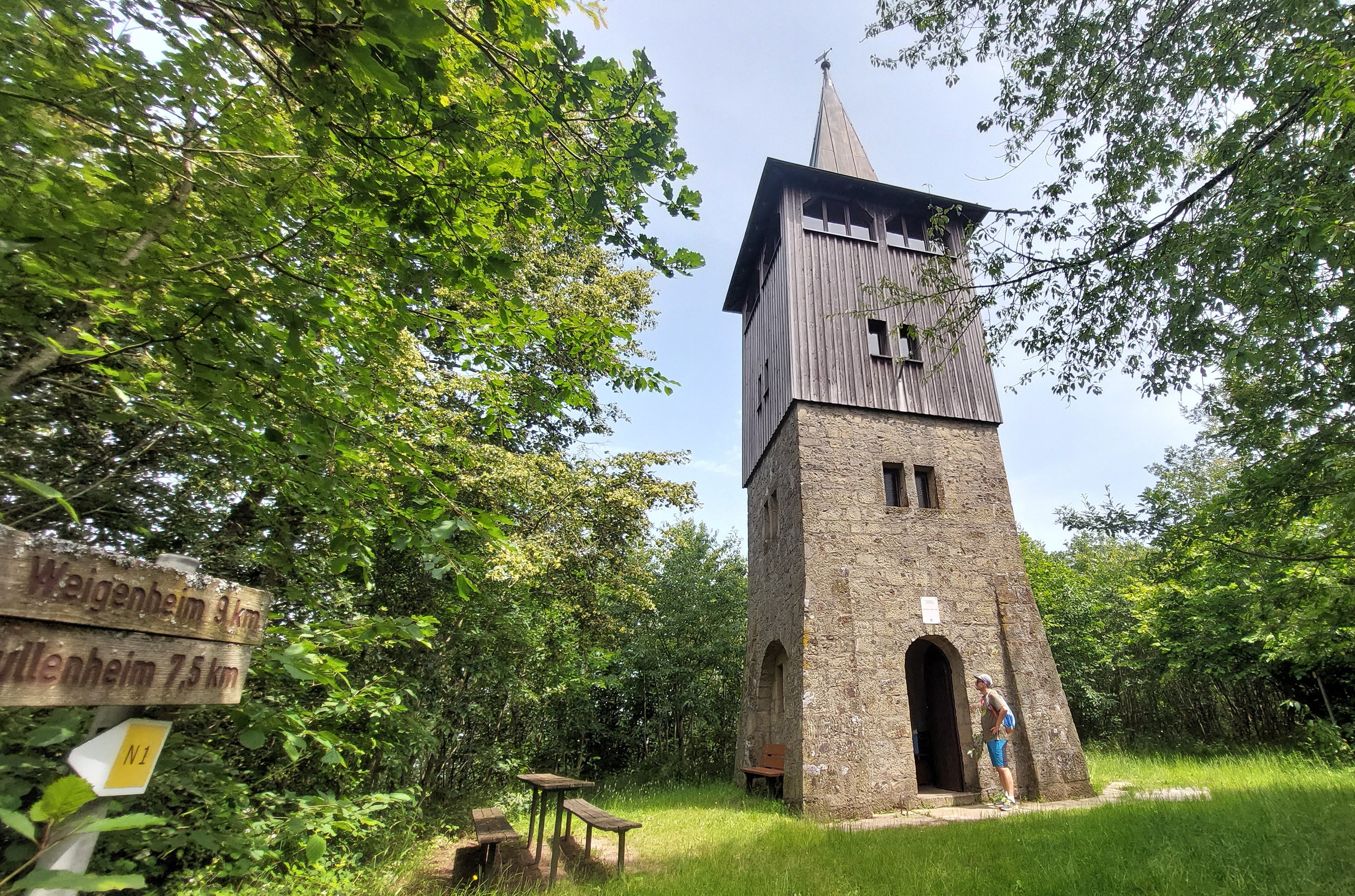 Andreas Därr Turm mit spitzen Dach auf einem kleinen Platz mit Wanderschildern Richtung Weigenheim