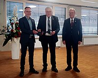 Drei Personen, einer davon übergibt einen großen Schlüssel