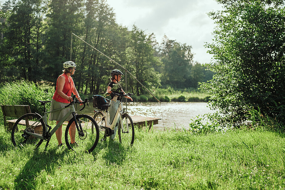 Zwei Radfahrer vor einem Teich inmitten grüner Natur