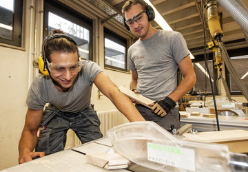 Zwei junge Männer bearbeiten in der Berufsschule Holz.