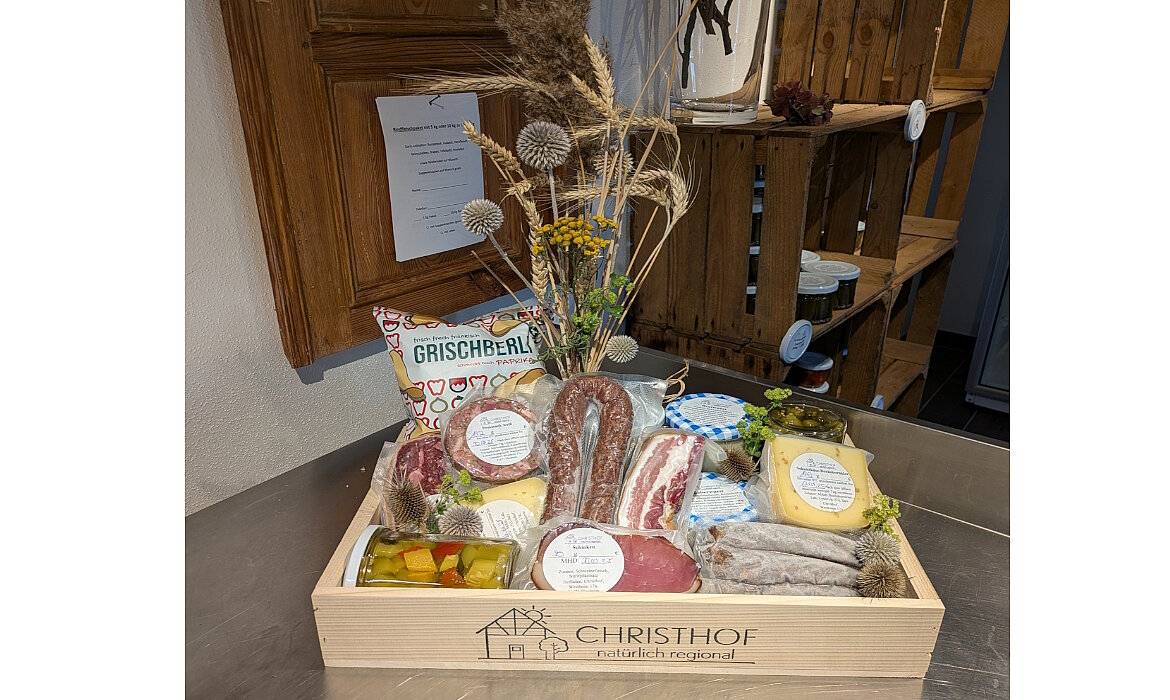 Ein Genusskorb voller Regionalität: Wurst, Käse, Eingelegtes und Spezialitäten wie „GRISCHERLI“ – liebevoll arrangiert im „CHRISTHOF“-Holzkistchen mit Trockenblumen verziert. Ein echtes Stück Heimat, das Qualität und Handwerk sichtbar macht.