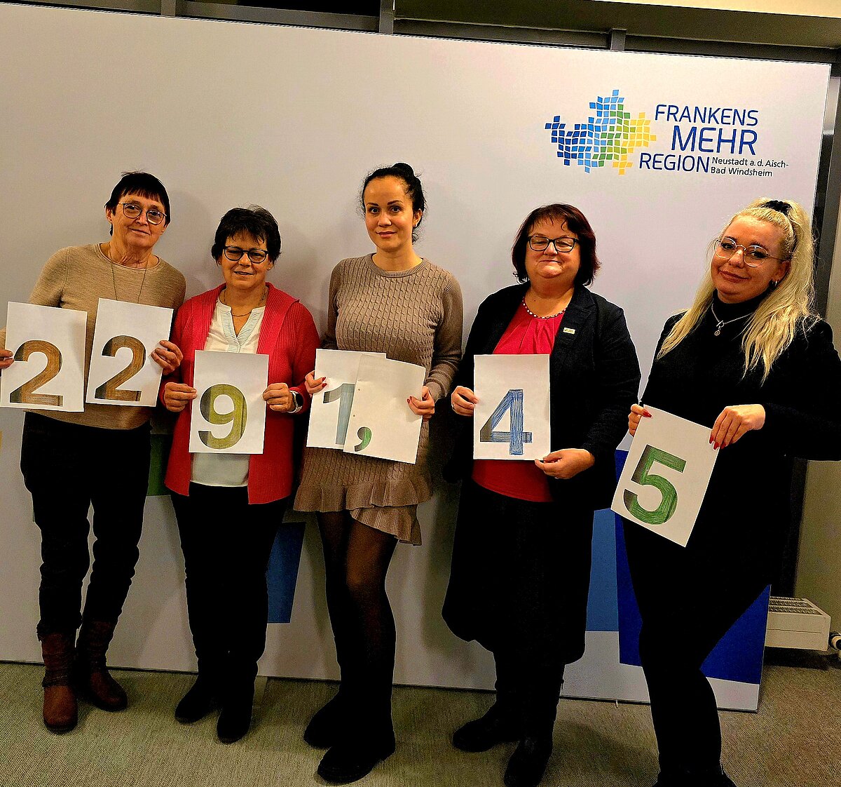 Fünf Personen stehen vor einem weißen Hintergrund mit dem Logo „Frankens MEHR Region“ und halten Blätter mit den Zahlen 2, 2, 9, 1, 4 und 5 in unterschiedlichen Farben.