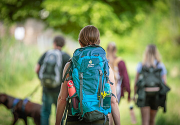 Vier Wanderer und ein Hund, Wanderin mit Rucksack von hinten im Fokus