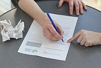 Jemand versucht ein Formular auszufüllen, jemand anderes hilft dabei