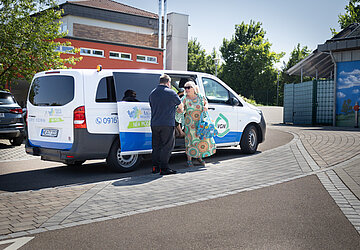 Nea Mobil Bus mit Personen die gerade aussteigen während der Fahrer die Tür aufhält 