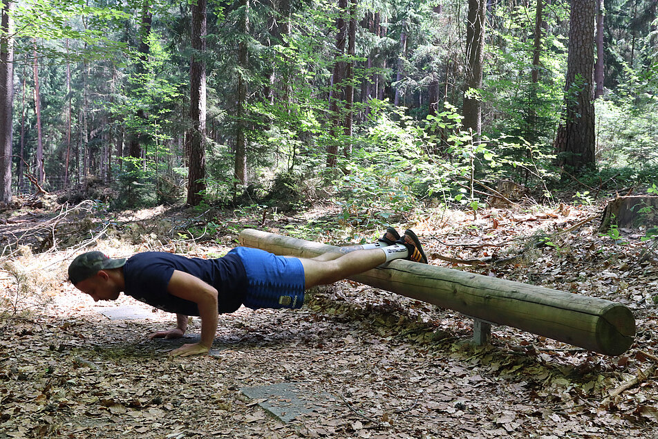 Eine person im Wald die an einem erhöten Holzbalken einen Stütz macht