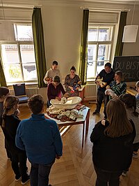 Menschen lernen mit Babypuppen und einem Beckenmodell in einem hellen Raum – vermutlich ein Geburtsvorbereitungskurs.