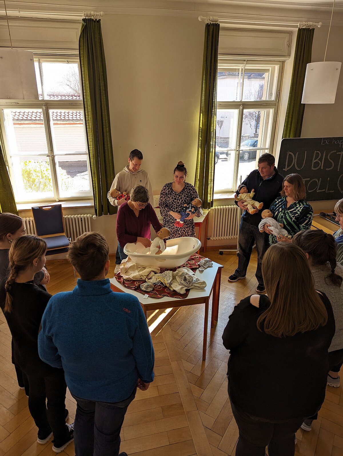 Menschen lernen mit Babypuppen und einem Beckenmodell in einem hellen Raum – vermutlich ein Geburtsvorbereitungskurs.