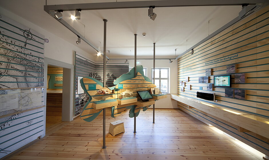 Ausstellungsraum im Karpfenmuseum mit einem großen Holzkarpfen in der Mitte in warmen Farben