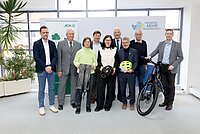 Neun Personen stehen mit Fahrradausstattung und einem E-Bike vor der Fotowand