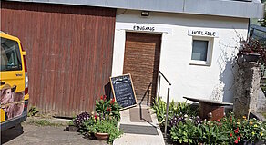 Einladender Hofladen-Eingang mit handgeschriebener Tafel: Frisches Fleisch vom Weiderind und Schwein, Grillpakete, Wurst, Käse, Eier, Milch, Joghurt, Eingemachtes, Nudeln, Marmelade, Honig, Säfte und Wein – ein echtes Schaufenster regionaler Vielfalt und bäuerlicher Qualität.