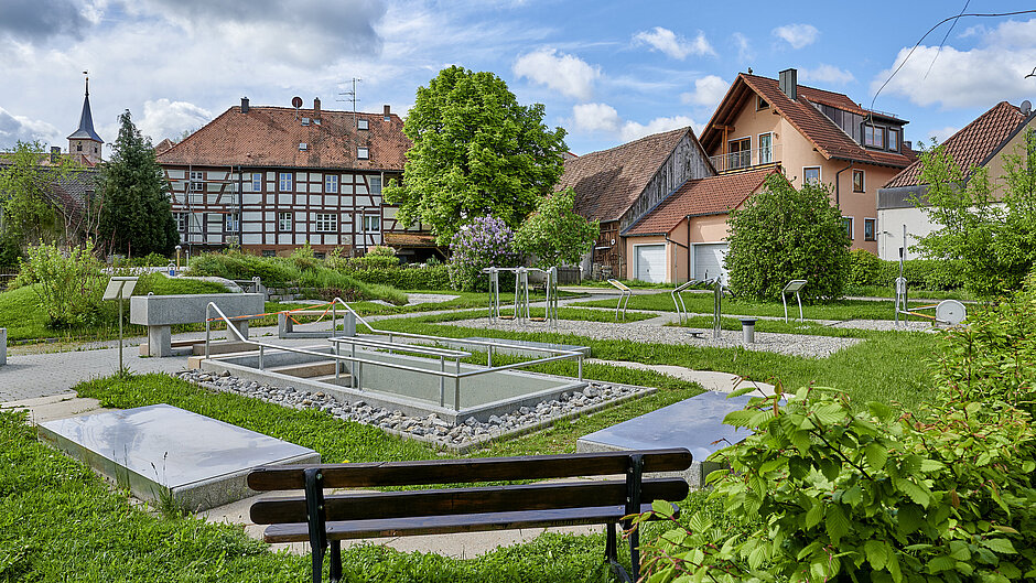 Bank im Vordergrund, Dorfpanorama von Münchsteinach im Hintergrund, dazwischen eine Kneippanlage und ein Wasserpark 