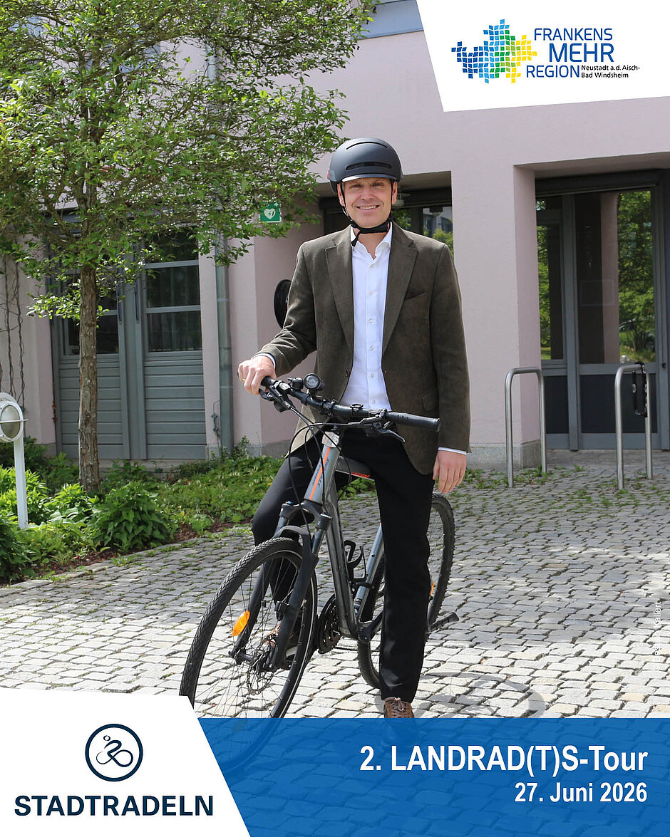 Landrat vor dem Landratsamt auf einem Fahrrad in sportlichen casual Outfit mit Schriftzug und Logo am unteren Rad des Bildes