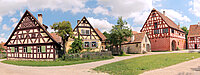 Dorfplatz Panorama, viele Fachwerkhäuser nebeneinander mit hellblauen mit wolken behangenem Himmel im Hintergrund