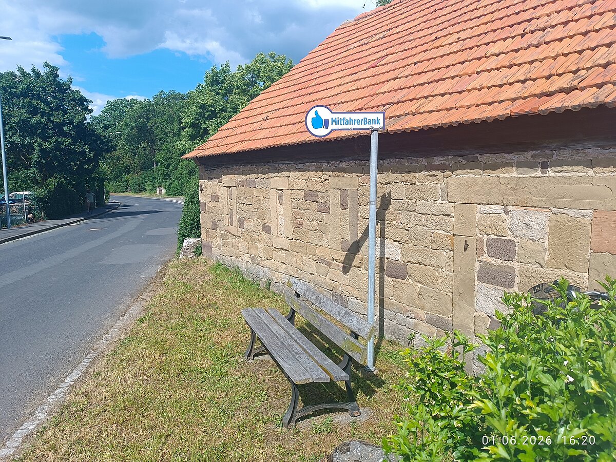 Bank mit Schild "Mitfahrbank" vor einer Hauswand