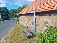 Bank mit Schild "Mitfahrbank" vor einer Hauswand