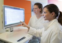 Zwei Personen in weißen Kitteln betrachten gemeinsam medizinische Daten auf einem Bildschirm in klinischer Umgebung.