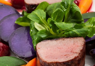 Zart rosa gebratenes Wildfleisch mit Gemüse und Feldsalat auf Teller angerichtet.