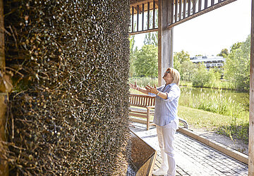 Eine Frau mit blonden Haaren streckt die Arme Richung gradierwerk, eine Strohähnliche Wand durch die die Sole fließt