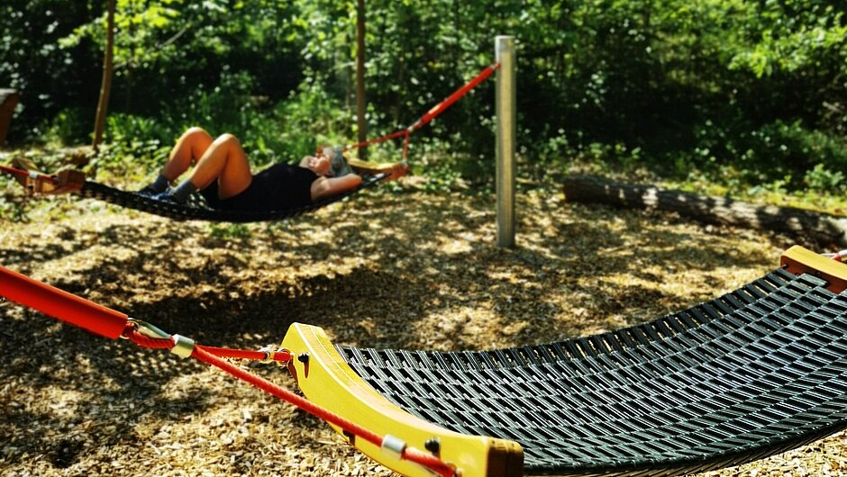 Waldbadeplatz_NEA_Lisa_Tiefel Zwei Hängematten im Wald mit einer Person die darauf liegt