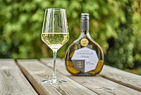 Glas Weißwein und bauchige Flasche mit der Aufschrift „Franken EWRICH Qualität“ auf einem Holztisch im Grünen.