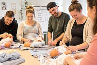 Eltern mit Babypuppen in einer Kurssituation.