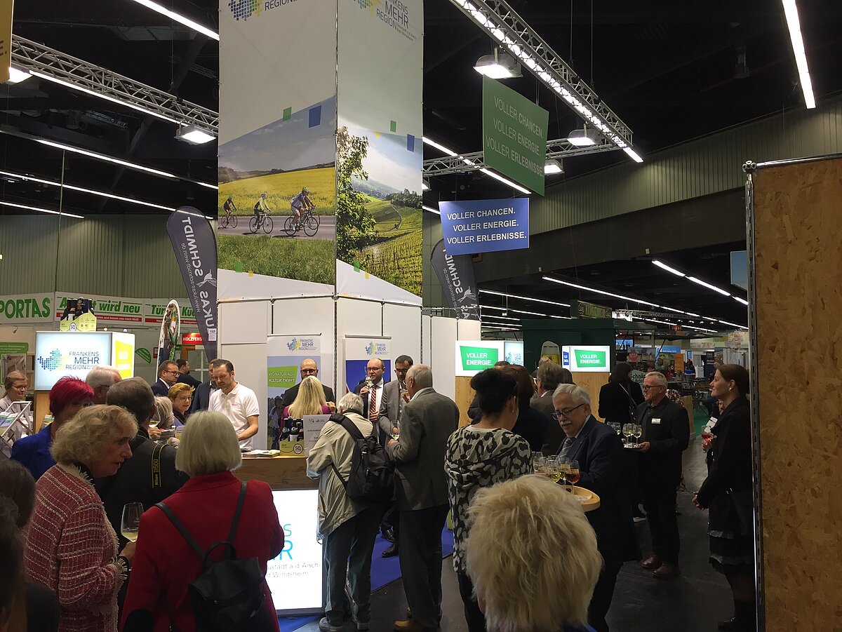 Messestand „Region Schwäbisch Hall“ auf Messe mit großem Display landschaftlicher Motive und Slogan „Voller Charme, voller Energie, voller Erlebnisse“ – Besucher tauschen sich aus, probieren Produkte und sammeln Informationen zu Freizeit und Tourismus in der Region.