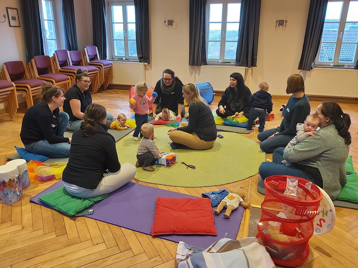 Mütter mit Kindern sitzen am Boden im Kreis