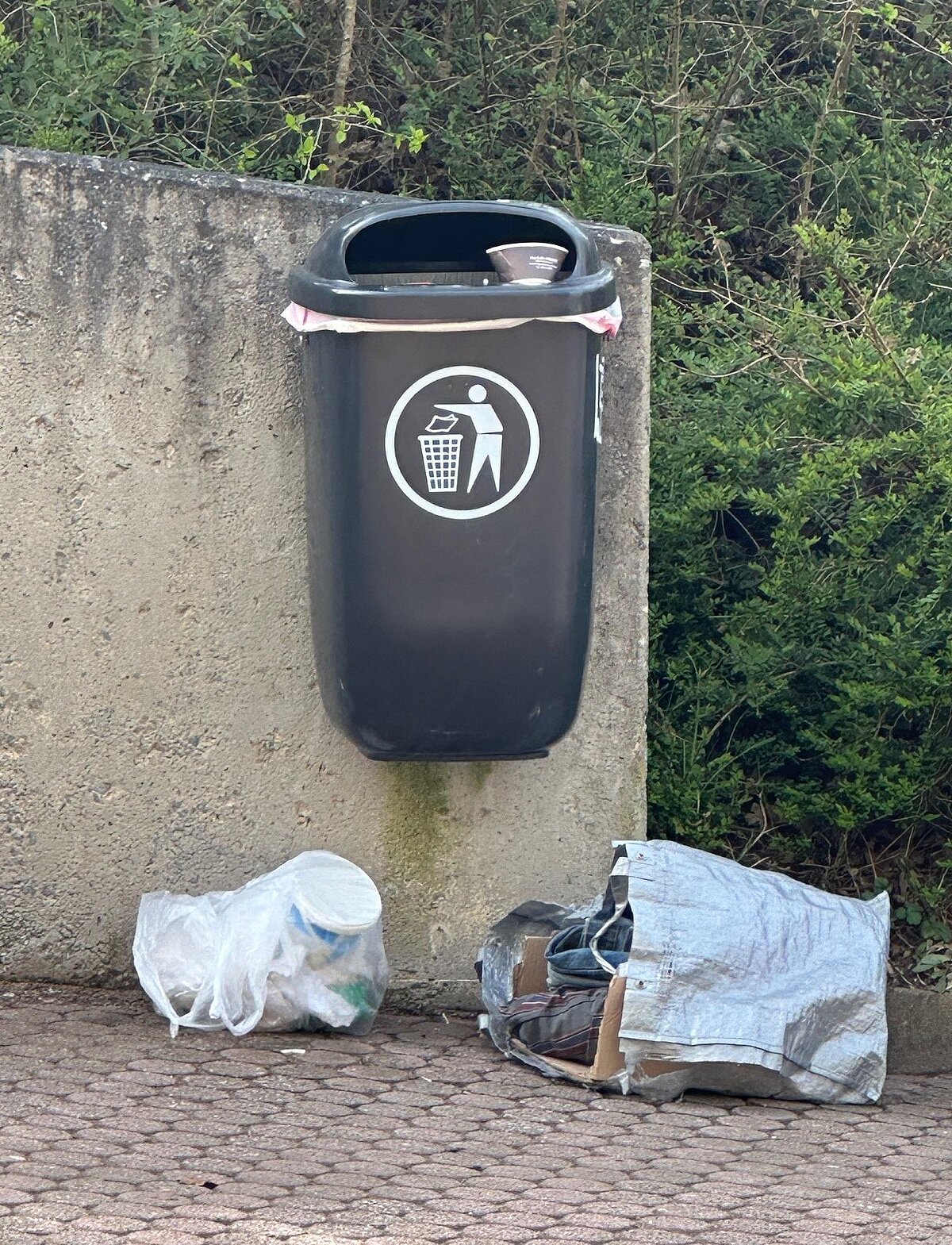 Öffentlicher Mülleimer, neben dem weitere Tüten mit Müll abgelagert wurden