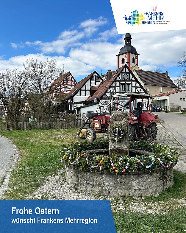 Osterbrunnen vor einem Kirchturm und Fachwerkhäusern