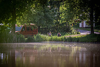 Zwei Personen im Campingstuhl vor einem Weiher mit Camper daneben 