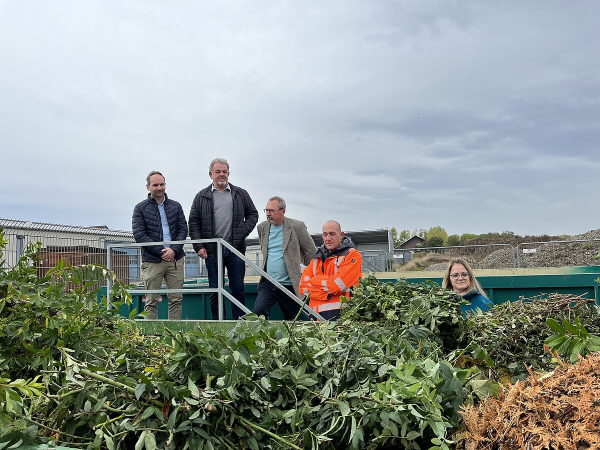 Fünf Personen sehen in einen Grüngutcontainer hinwein
