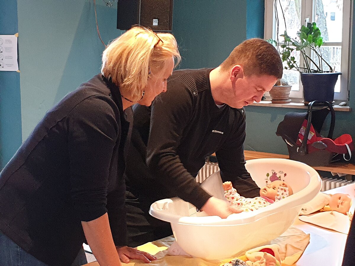 Eine Frau und ein Mann baden eine Babypuppe