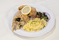 Ein ganzer gebratener Karpfen mit Zitronenscheibe, Kartoffelpüree mit Schnittlauch und Beilagensalat auf einem weißen Teller.