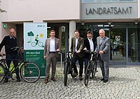 Fünf Personen stehen mit Fahrrädern vor dem Eingang des Landratsamts neben einem grünen Banner der AOK mit der Aufschrift „Mit dem Rad zur Arbeit“.