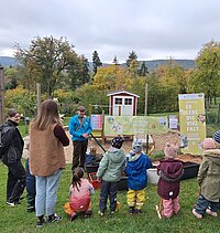 Kinder und drei Erwachsene stehen vor verschiedenen Wannen mit Erde