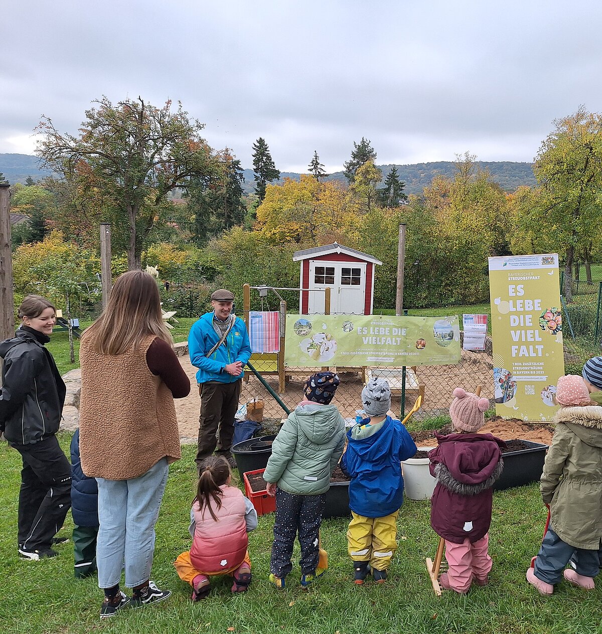 Kinder und drei Erwachsene stehen vor verschiedenen Wannen mit Erde