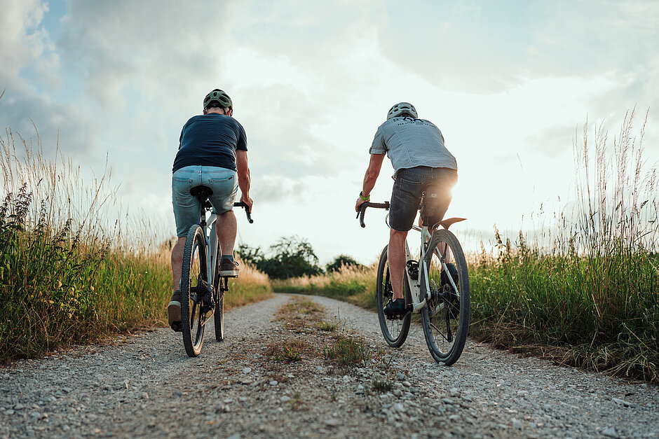 Radfahrer Sonnenuntergang Zwei Radfahrer von hinten auf einem Schotterweg im Sonnenuntergang