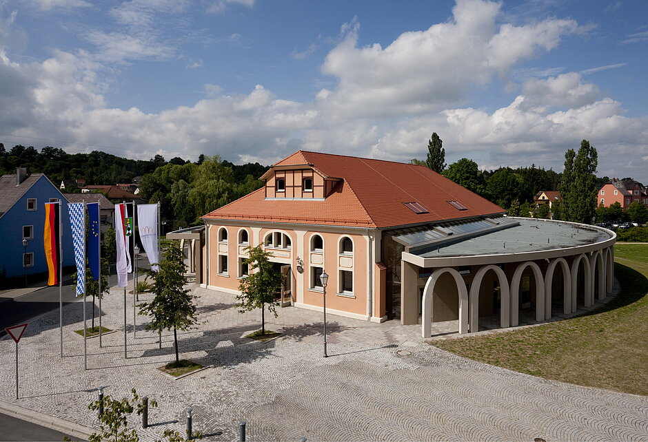 Luftaufnahme von der NeuStadtHalle. Das Gebäude hat außen runde Bögen und hat die Farbe Orange sowie ein orangenes Dach. 