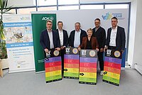 Sechs Personen stehen vor einem weißen Hintergrund mit dem Logo „Frankens MEHR Region“ sowie zwei Roll-Up-Bannern der Gesundheitsregionplus und AOK, und halten jeweils ein großes farbiges Schild mit der Überschrift „UV INDEX“ und einer Skala von 1 bis 11+.