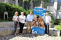 Vier Personen stehen im Freien neben einem blauen Banner mit der Aufschrift „freilich Deine Plattform für Engagement in Bayern“, das zusätzlich ein Foto von mehreren Menschen und weitere Textinformationen enthält.