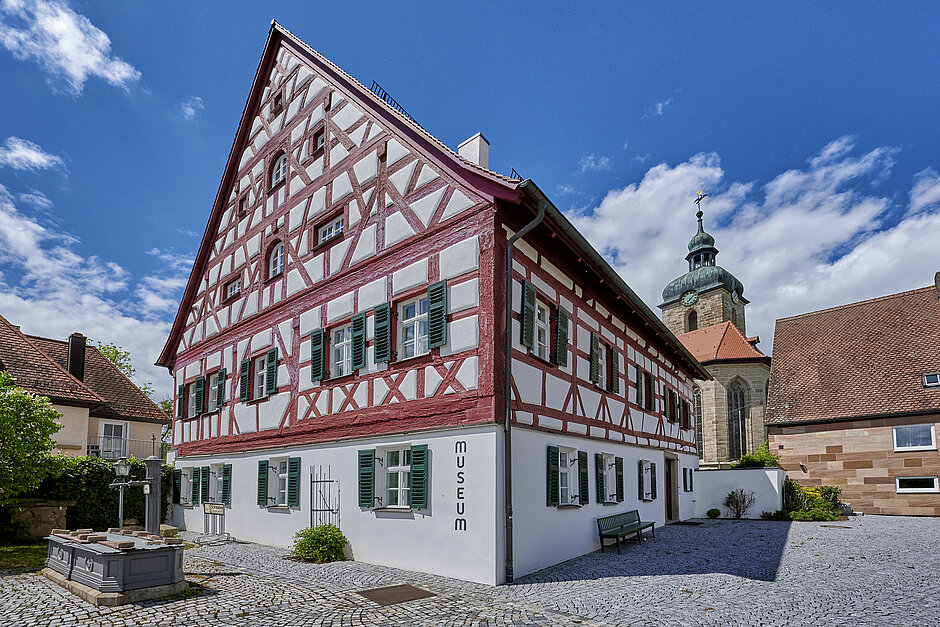 Weißes Fachwerkhaus im Innenort mit rotem Fachwerk vor einer Kirche