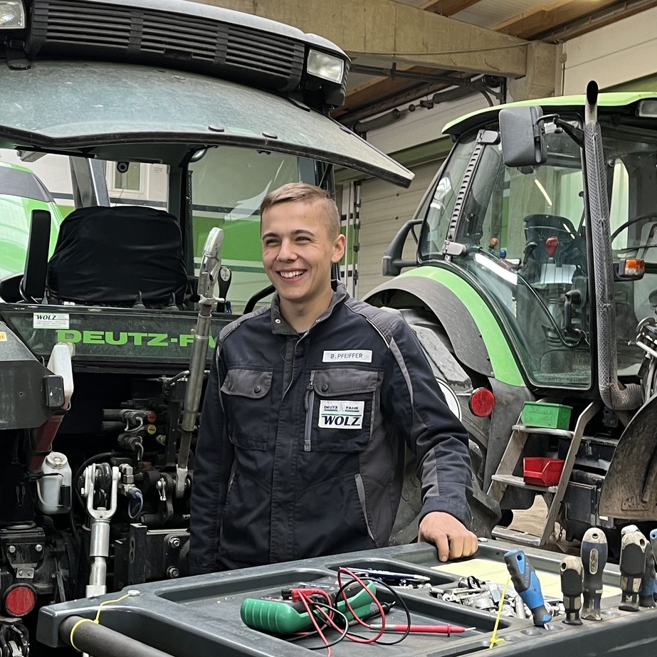 Benjamin Azubi WOLZ -Landtechnik - in Arbeitskleidung vor dem Traktor 