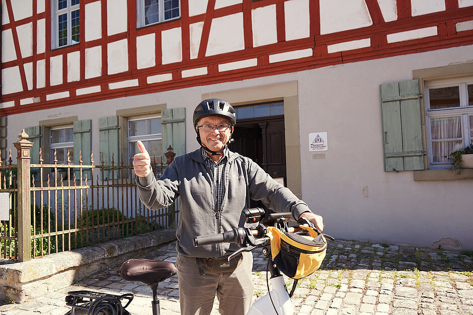 STADTRADELN Star Harald Trabert Ein älterer Mann vor einem Fachwerkhaus mit Daumen nach oben vor seinem Fahrrad.