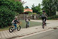 Zwei Kinder auf dem Weg zum Kindergarten mit ihrer Mutter. Alle fahren Rad. 