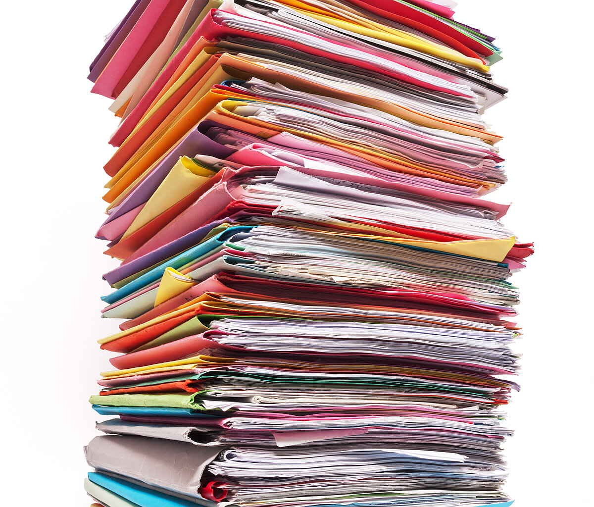 Riesiger Stapel mit bunten Mappen, aus denen Papier quillt