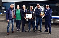 Personen vor Flugzeug mit Überreichung Defibrillator