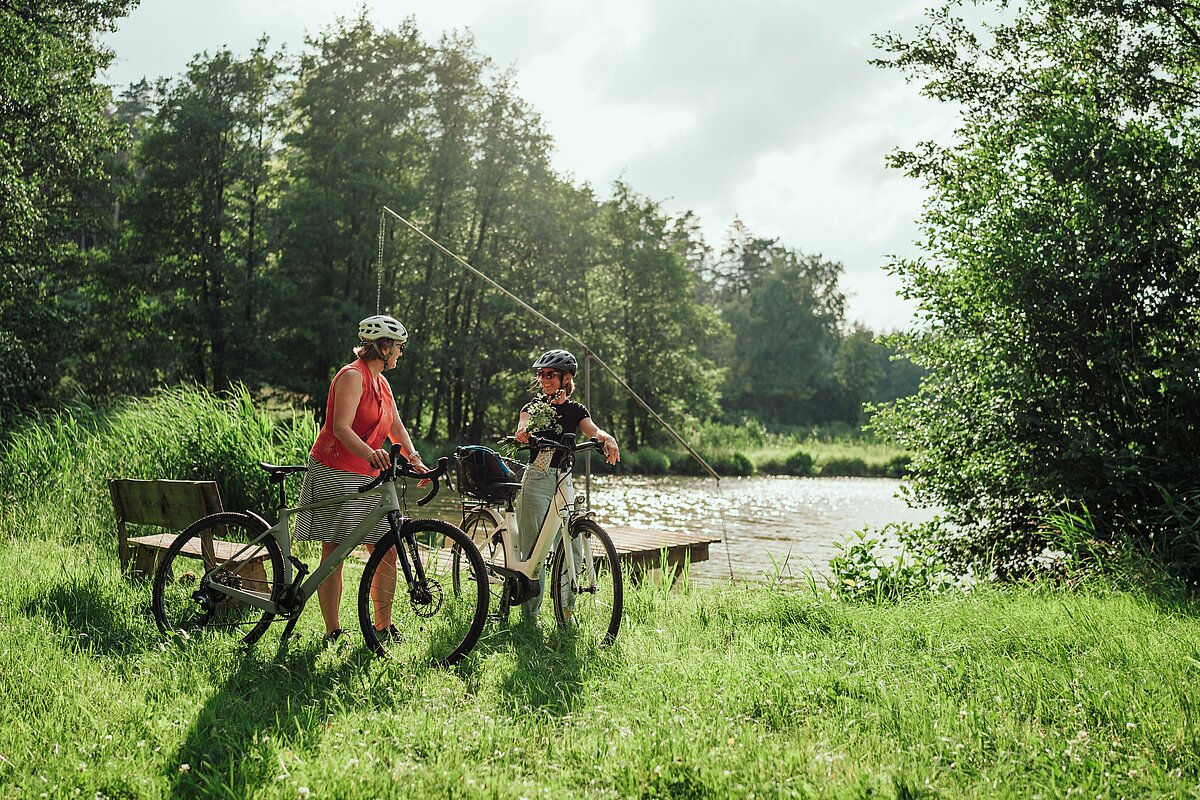 Zwei Radfahrerinnen vor einem Weiher 