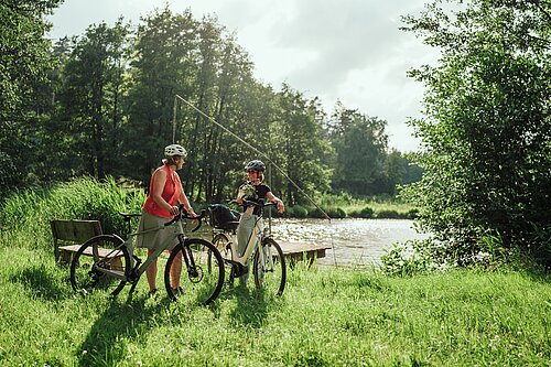 Zwei Radfahrerinnen vor einem Weiher 